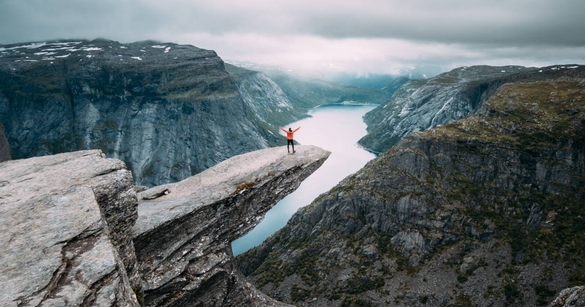 Man met zijn handenin de lucht van blijdschap op de beroemde rots van Trolltunga in Noorwegen.